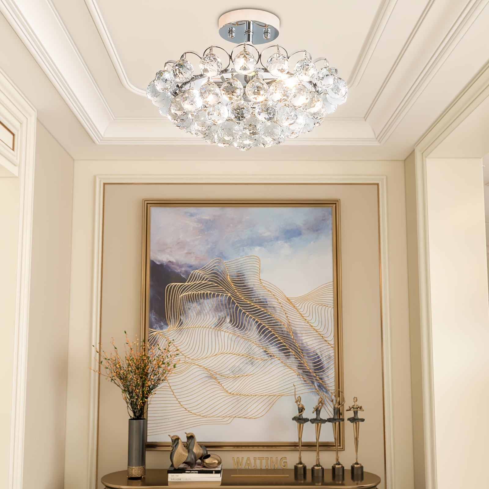 A display table with sculptures and a gold-framed abstract painting beneath a crystal bubble light fixture mounted on the ceiling