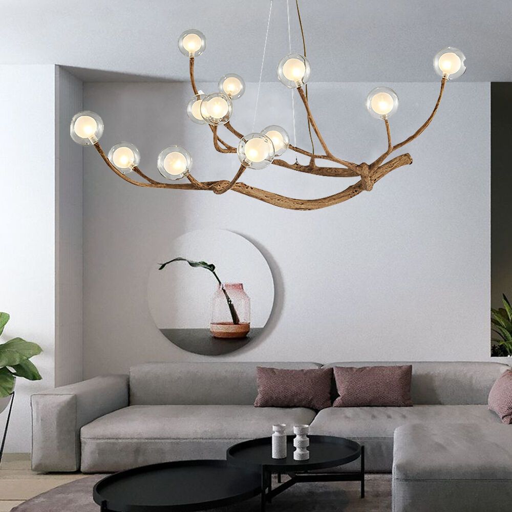 Contemporary chandelier with branch-style arms and glass globes hanging over a neutral-toned sofa set with round black tables and wall art in a stylish interior