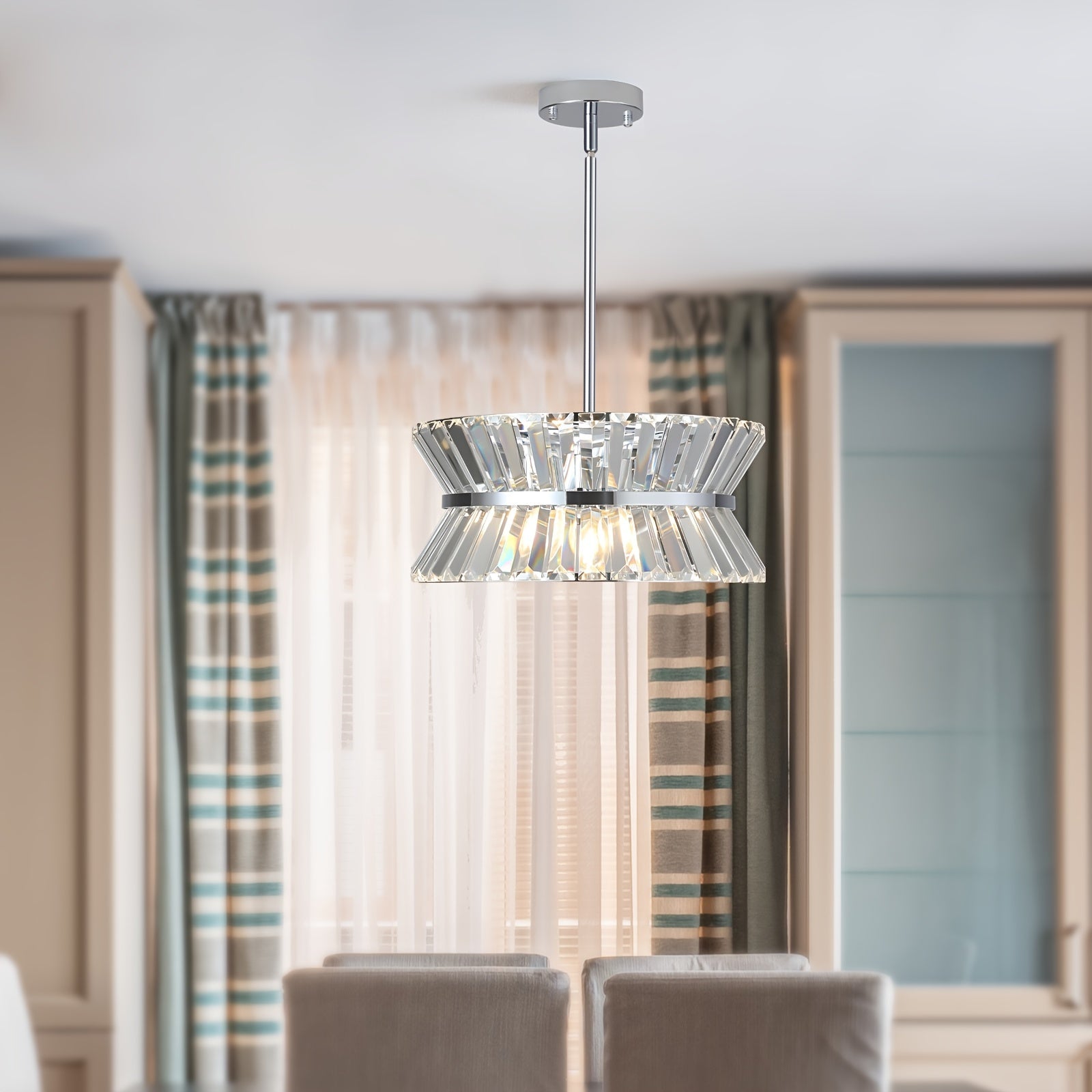 Semi flush crystal chandelier installed above a soft-toned dining space with striped curtains and cushioned chairs