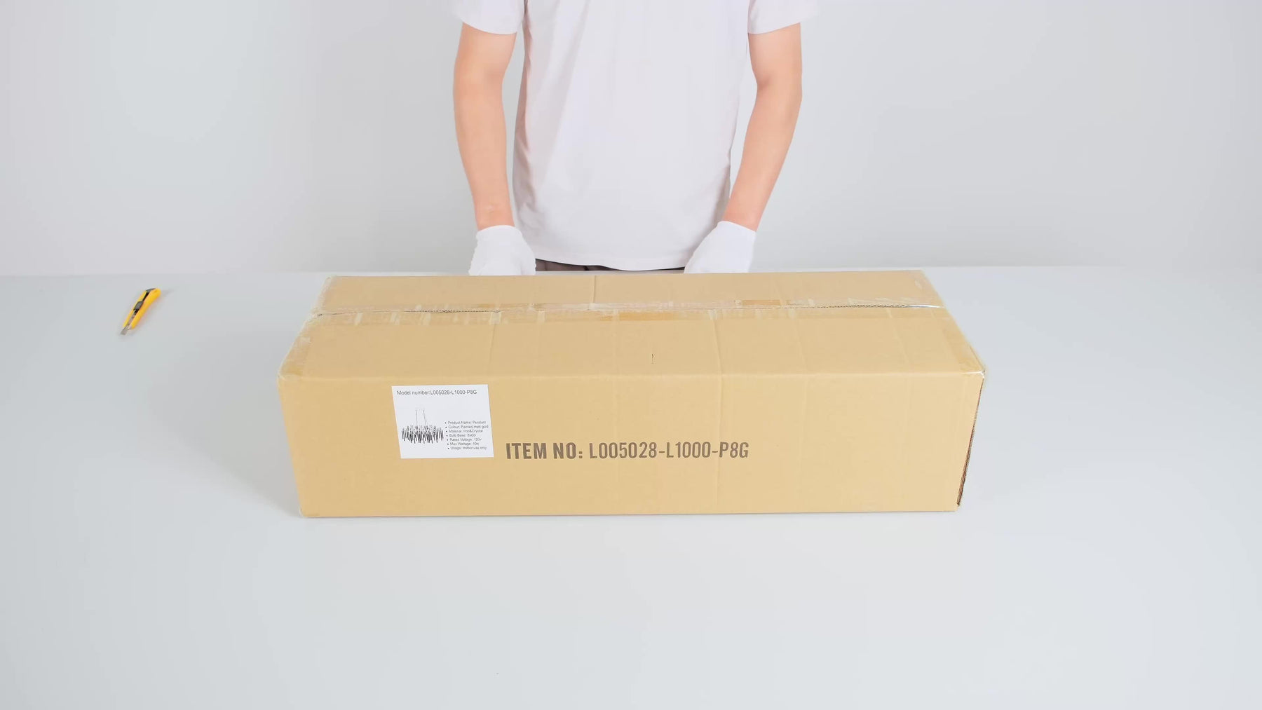 Shipping box with product label for gold crystal dining chandelier, placed on a white surface with a person ready to open the package