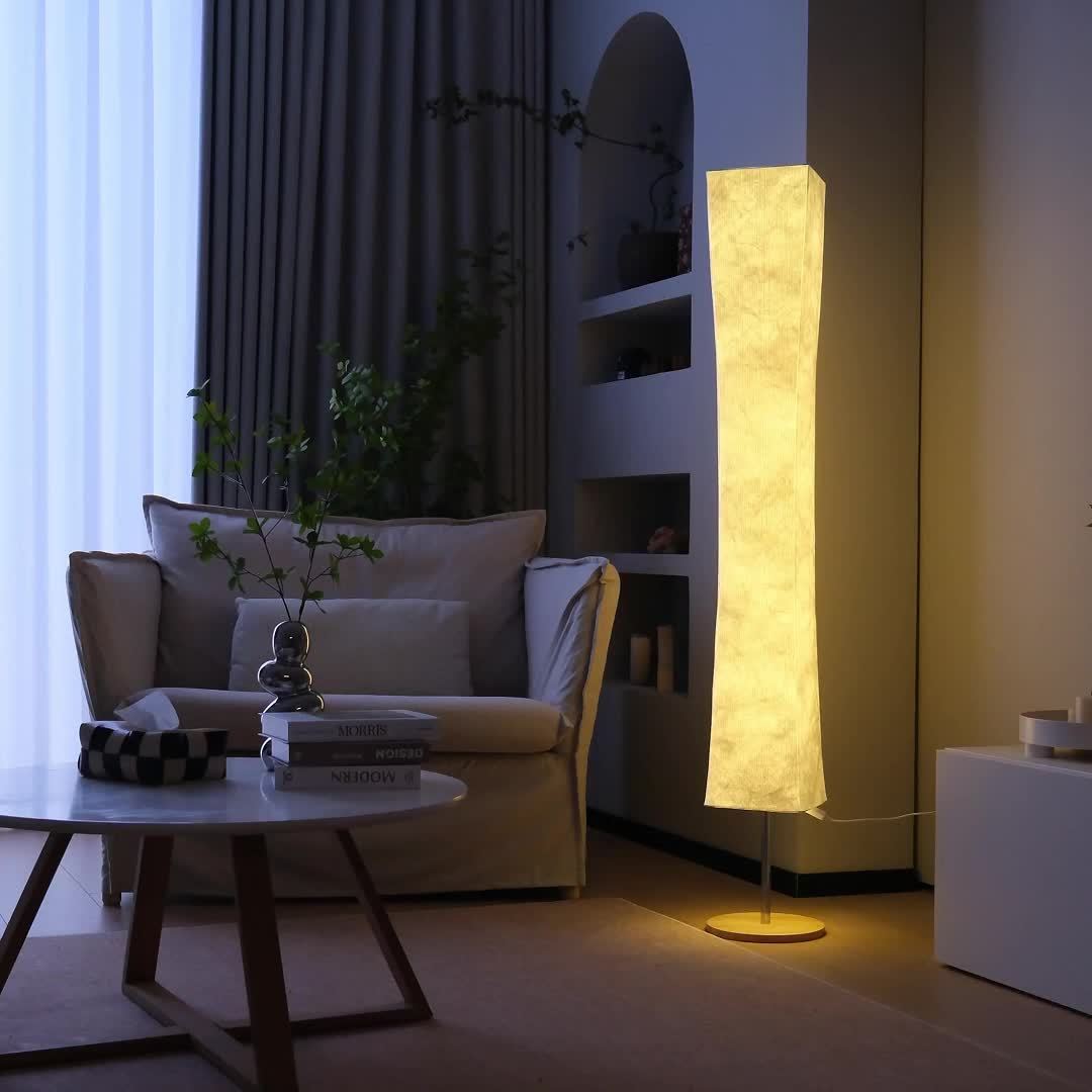 An illuminated standing lamp with a unique textured shade, providing soft, warm ambient light to a cozy room with a sofa and subtle decor
