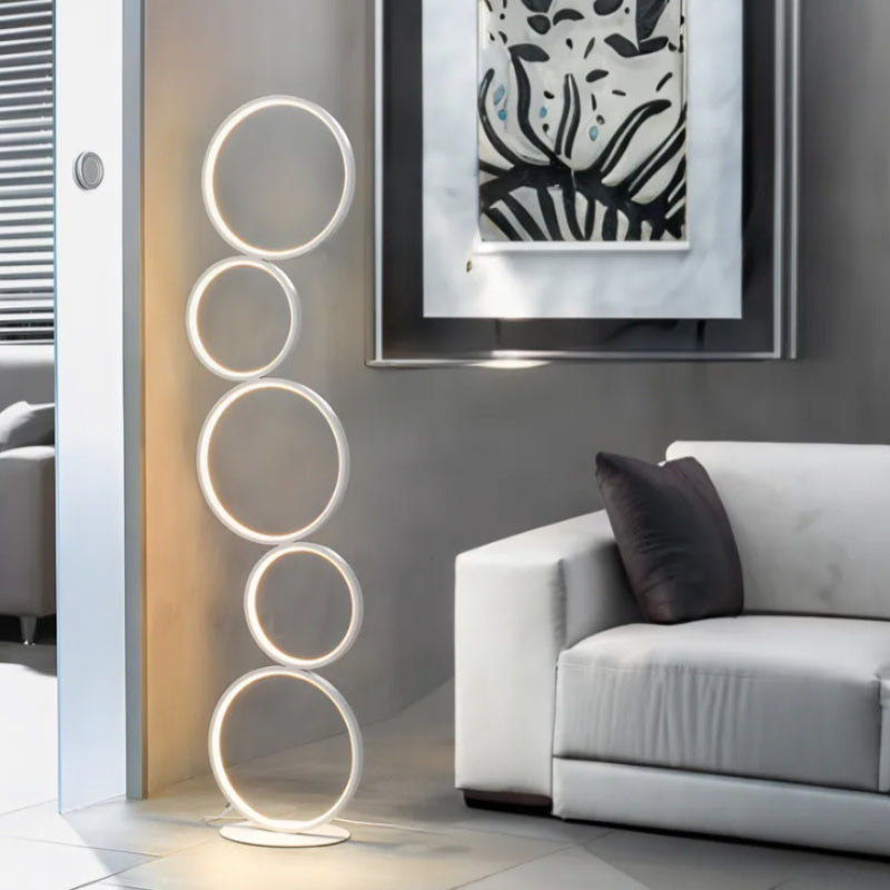 Modern seating space accented by a circular floor lamp with five illuminated white rings placed beside a framed wall art