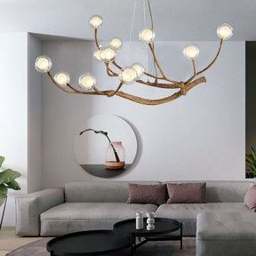 Contemporary chandelier with branch-style arms and glass globes hanging over a neutral-toned sofa set with round black tables and wall art in a stylish interior