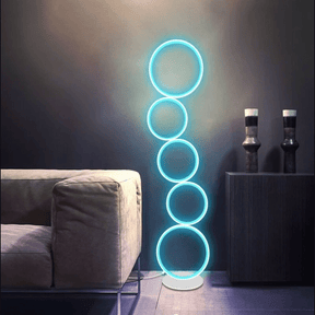Contemporary room accented by a circular floor lamp with five glowing blue rings, placed between a soft couch and dark cabinet