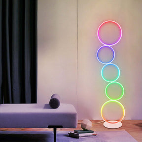 Colorful ambient space featuring an RGB circular floor lamp with five glowing rings in gradient colors, placed near a modern lounge chair