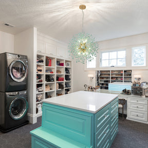 Elegant dandelion chandelier suspended above turquoise island drawers in a modern walk-in closet with open shelving