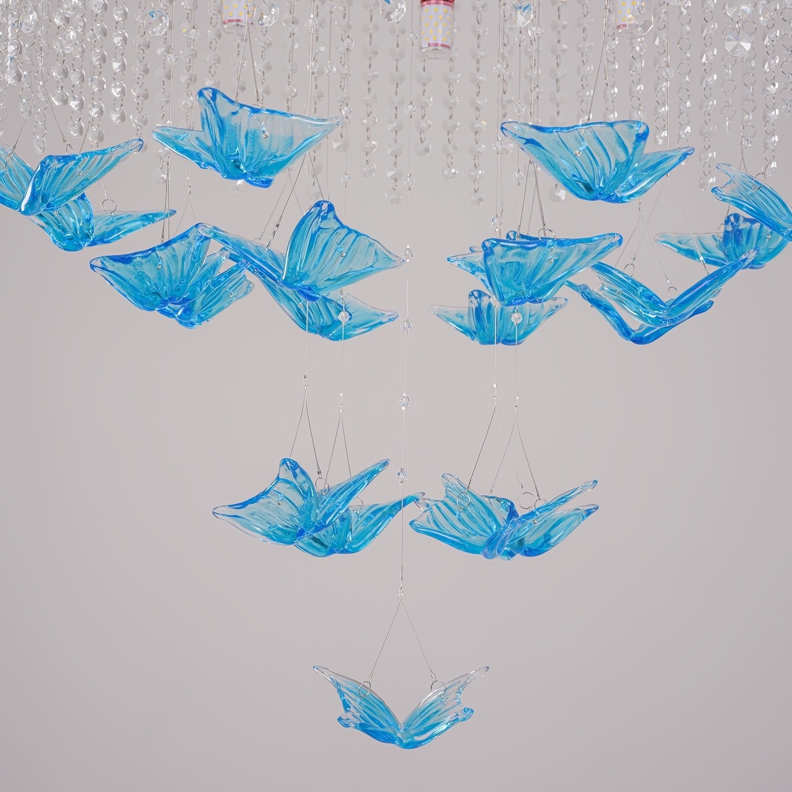 Blue glass butterflies suspended on transparent strings beneath crystal strands, designed as part of a hanging decorative light
