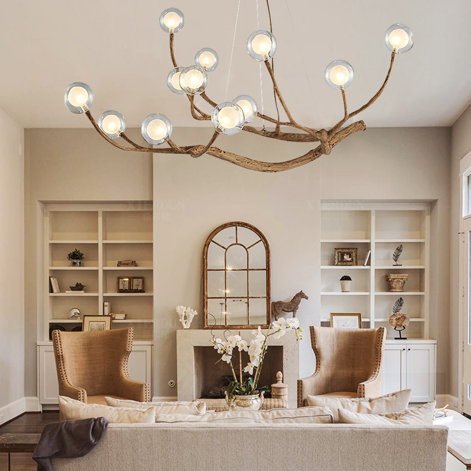 Branch-style chandelier with round glass bulbs, suspended above a warm-toned seating area with fireplace and armchairs