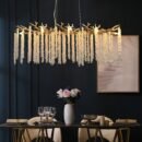 Crystal branch chandelier above a modern dining table with gold accents and dark wall backdrop
