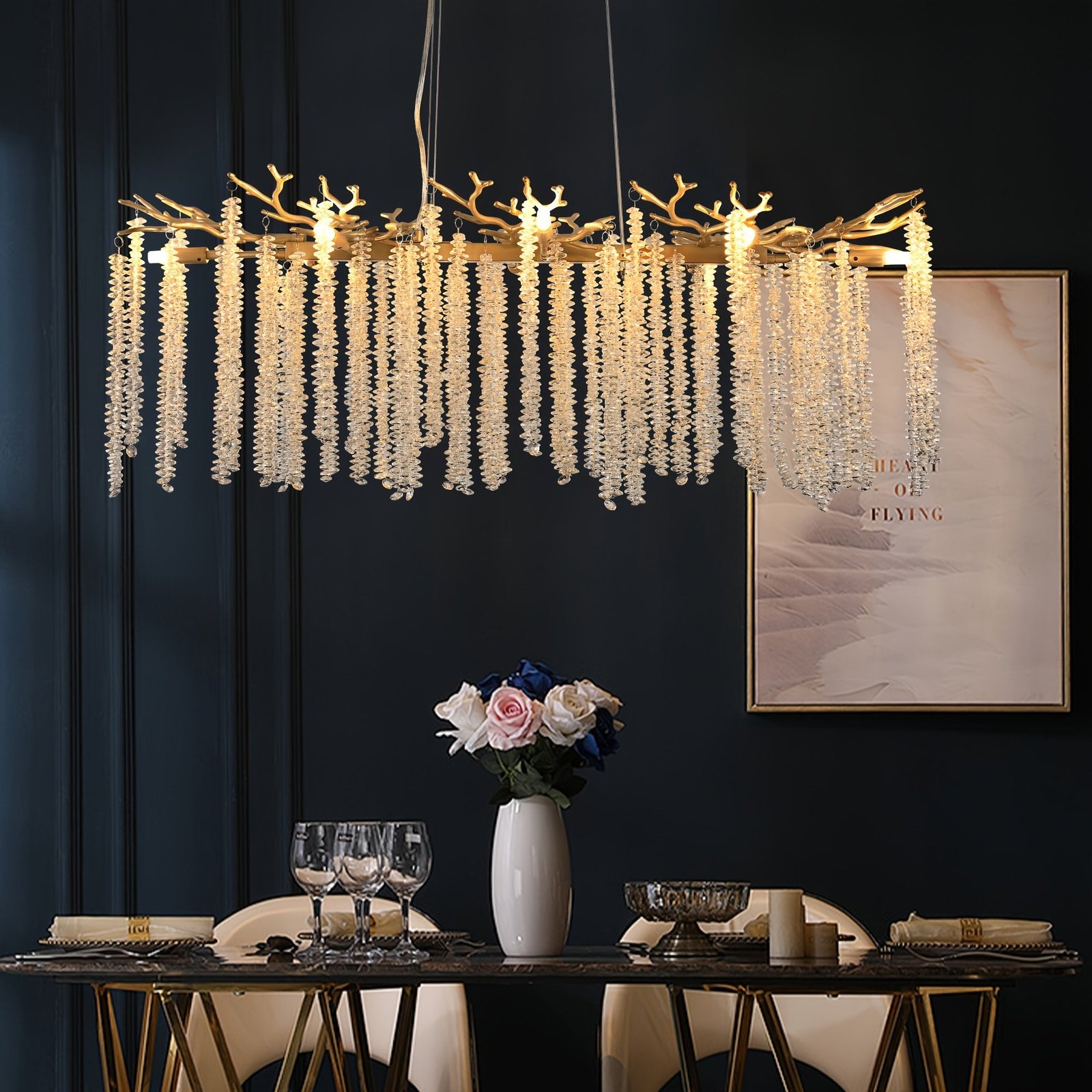 Crystal branch chandelier above a modern dining table with gold accents and dark wall backdrop