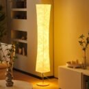 Tall modern floor lamp with soft fabric shade, emitting a warm ambient glow in a cozy corner with neutral decor and indoor plants