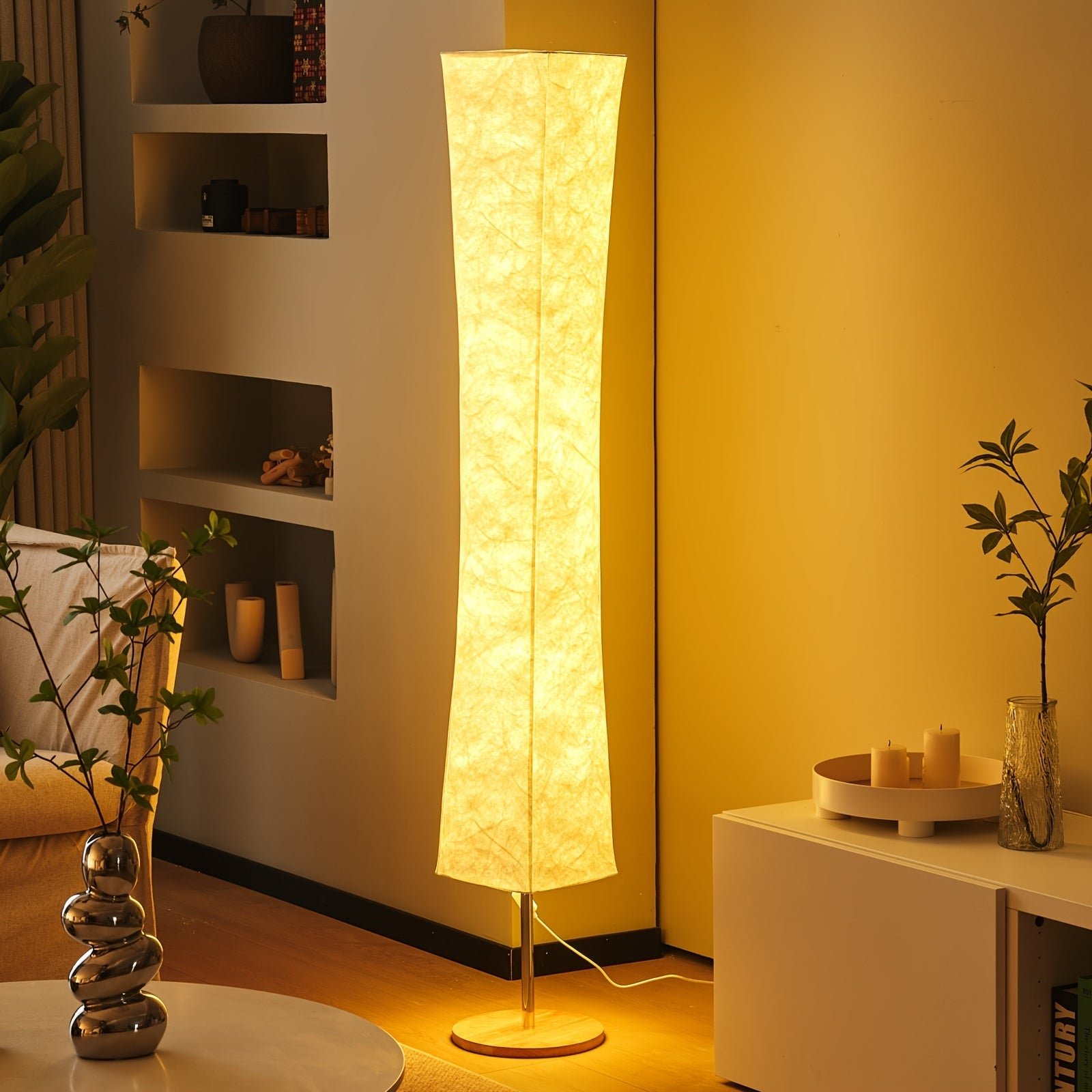 Tall modern floor lamp with soft fabric shade, emitting a warm ambient glow in a cozy corner with neutral decor and indoor plants